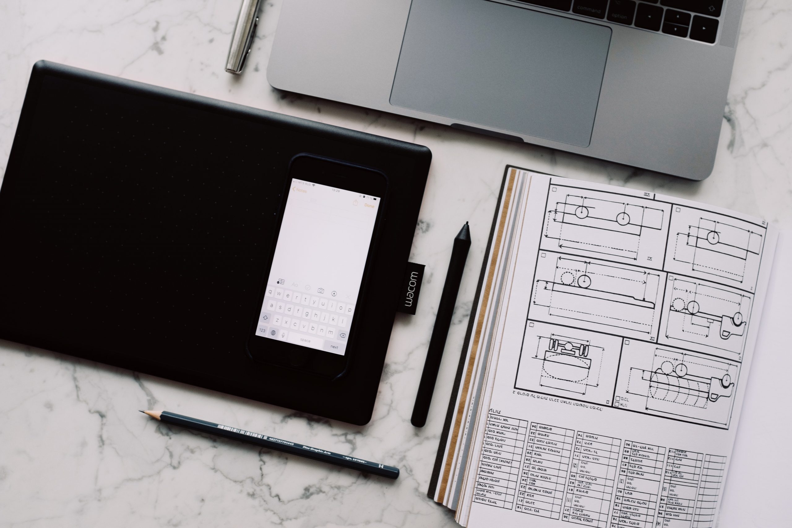 A black notepad, a laptop, and a pensil-drawn sketch on the table.